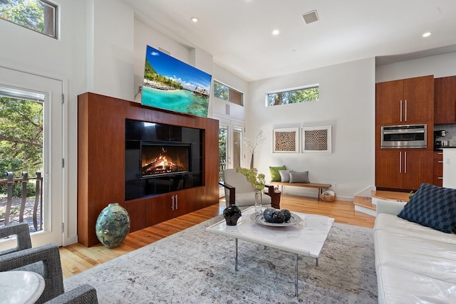 living area with light wood-style flooring, plenty of natural light, a tile fireplace, recessed lighting, and a high ceiling
