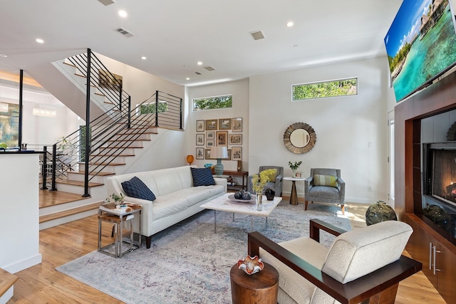 living room featuring recessed lighting, visible vents, stairway, a high ceiling, and wood finished floors