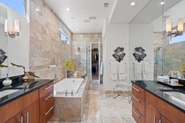 full bath featuring a stall shower, plenty of natural light, a bath, two vanities, and recessed lighting