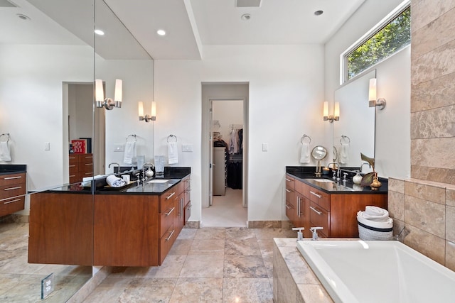 bathroom with two vanities, tiled bath, a walk in closet, and baseboards