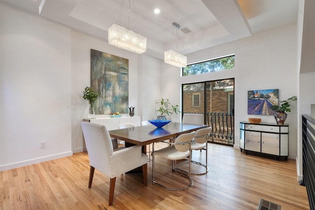 dining space featuring light wood finished floors, visible vents, baseboards, a tray ceiling, and a chandelier