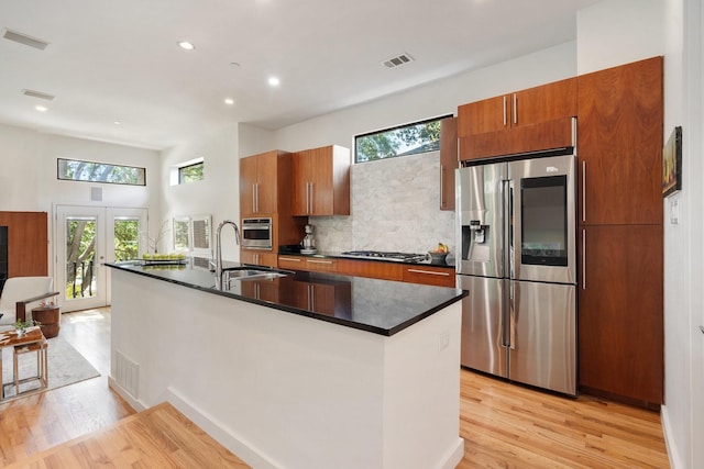 kitchen with appliances with stainless steel finishes, a sink, light wood-style flooring, dark countertops, and plenty of natural light