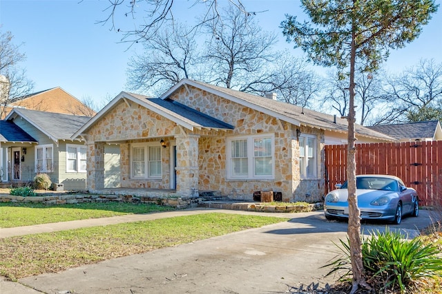 view of front of property featuring concrete driveway, stone siding, a chimney, fence, and a front yard