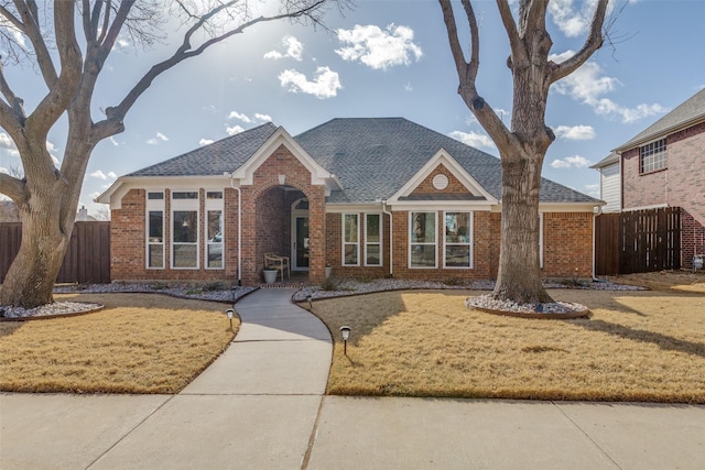 view of front of house featuring brick siding, a front lawn, and fence