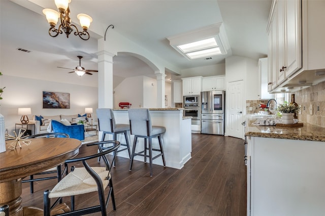 kitchen featuring arched walkways, decorative columns, tasteful backsplash, appliances with stainless steel finishes, and a ceiling fan