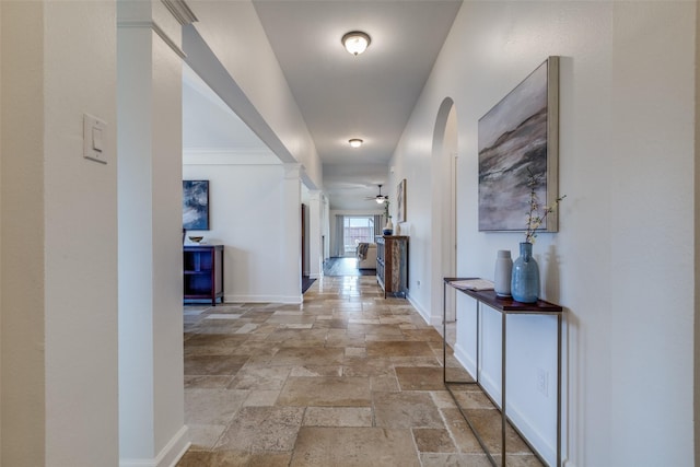 hall featuring decorative columns, baseboards, arched walkways, and stone tile flooring