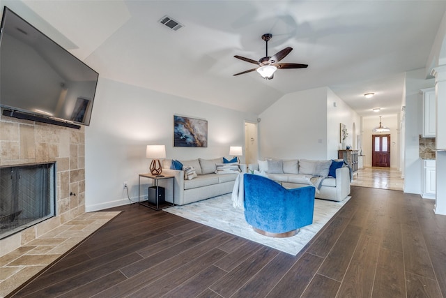 living area featuring visible vents, vaulted ceiling, a tiled fireplace, and wood finished floors