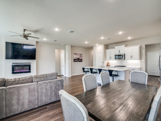 dining area featuring visible vents, a glass covered fireplace, dark wood-type flooring, and recessed lighting