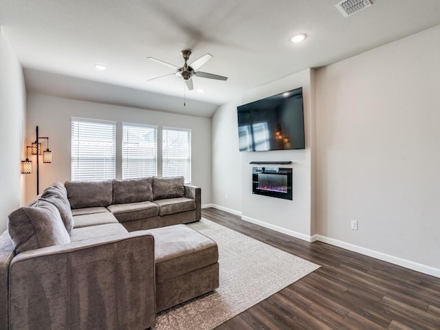 living room featuring dark wood-type flooring, a ceiling fan, visible vents, baseboards, and a glass covered fireplace