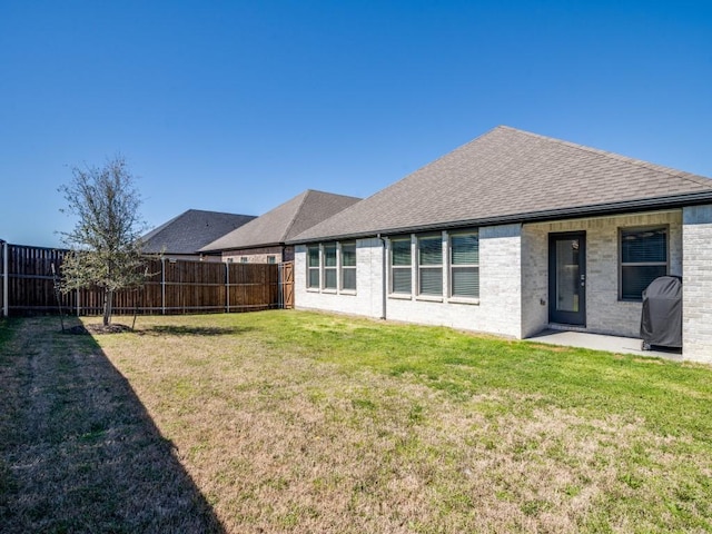 back of property featuring brick siding, a fenced backyard, a shingled roof, and a yard