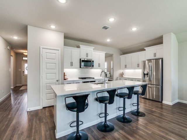 kitchen with visible vents, an island with sink, a sink, stainless steel appliances, and backsplash