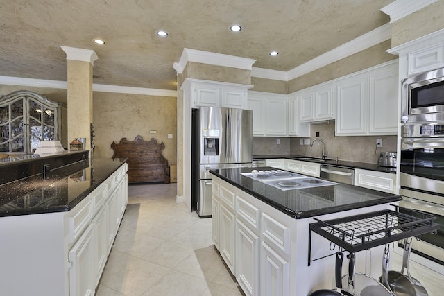 kitchen with appliances with stainless steel finishes, ornamental molding, dark stone countertops, white cabinetry, and a sink