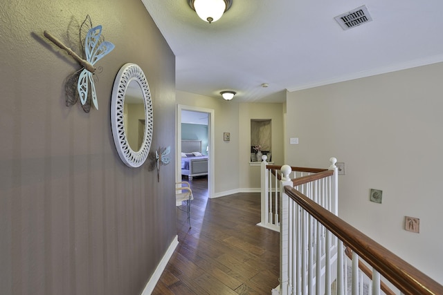 hall with baseboards, visible vents, dark wood-style flooring, crown molding, and an upstairs landing