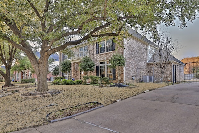 view of front facade with cooling unit, brick siding, fence, driveway, and a gate