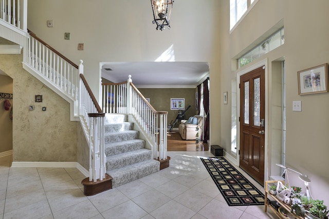 foyer featuring baseboards, a towering ceiling, stairway, ornamental molding, and tile patterned floors