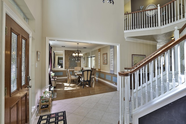 tiled entryway featuring stairs, a high ceiling, ornamental molding, and a notable chandelier