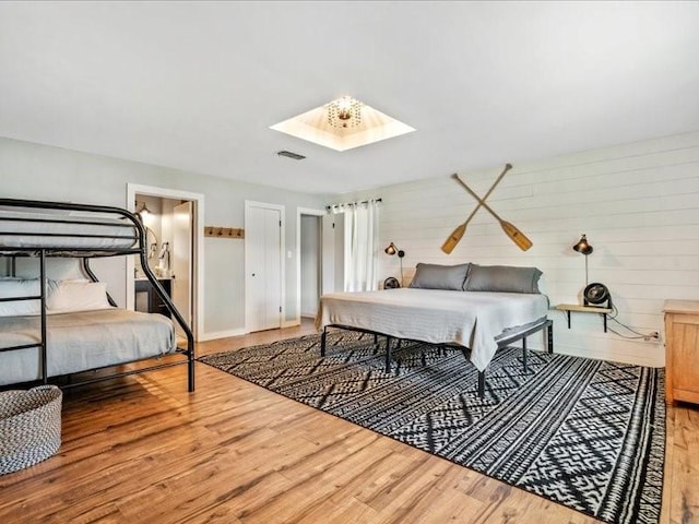 bedroom with a skylight, wooden walls, visible vents, and wood finished floors