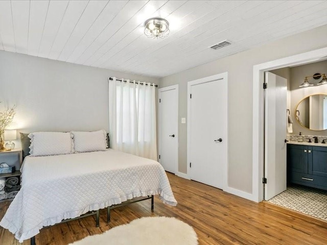 bedroom featuring visible vents, light wood-style flooring, connected bathroom, a sink, and baseboards