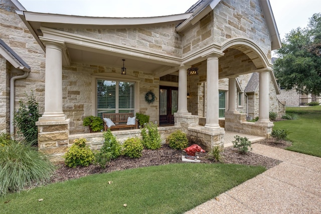 view of exterior entry with covered porch, stone siding, and a yard