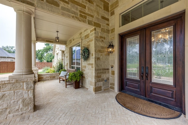 property entrance with covered porch, stone siding, french doors, and fence