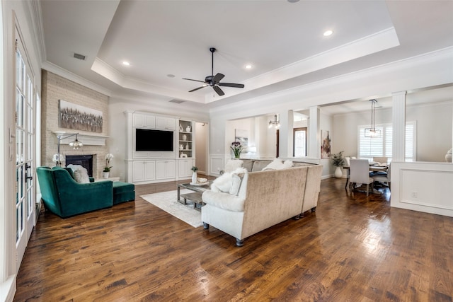 living room with dark wood-type flooring, a brick fireplace, and a raised ceiling