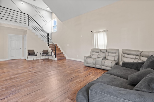 living area with wood finished floors, a towering ceiling, baseboards, and stairs