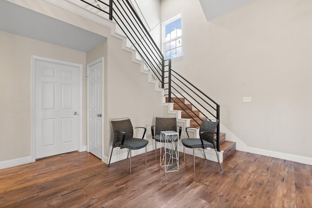 staircase featuring a towering ceiling, baseboards, and wood finished floors