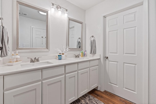 bathroom with double vanity, visible vents, a sink, and wood finished floors