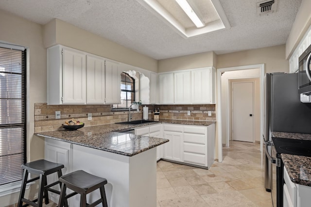 kitchen featuring visible vents, dark stone counters, a peninsula, white cabinetry, and a sink