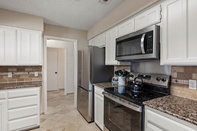 kitchen featuring a textured ceiling, stainless steel appliances, dark stone counters, white cabinets, and decorative backsplash