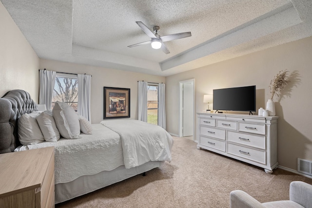 bedroom featuring visible vents, a textured ceiling, baseboards, a raised ceiling, and light colored carpet