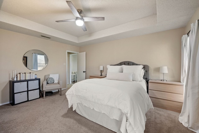 bedroom with visible vents, a textured ceiling, carpet floors, a raised ceiling, and ceiling fan