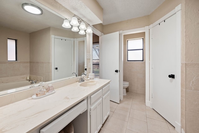 bathroom with tile patterned flooring, tile walls, toilet, vanity, and a textured ceiling