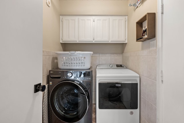 laundry area with washing machine and dryer, cabinet space, and tile walls