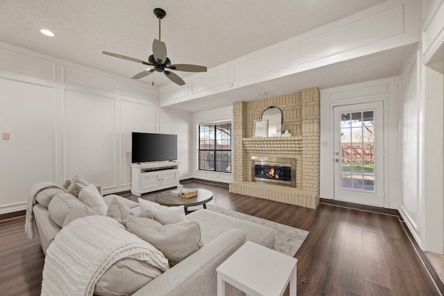 living room featuring dark wood-style floors, a decorative wall, a fireplace, and a healthy amount of sunlight