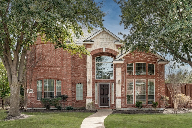 traditional home featuring stone siding, brick siding, a front lawn, and fence