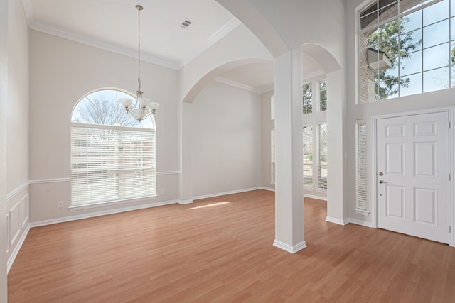 foyer entrance featuring light wood-style flooring, crown molding, a towering ceiling, baseboards, and an inviting chandelier