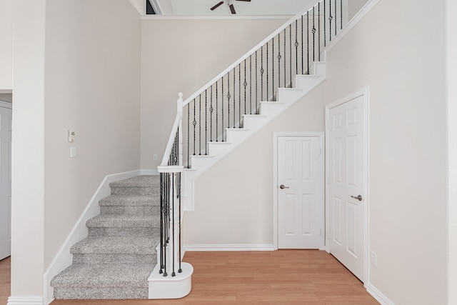 stairs featuring a towering ceiling, baseboards, and wood finished floors