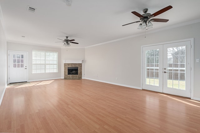 unfurnished living room with light wood-style floors, ornamental molding, a tiled fireplace, and french doors