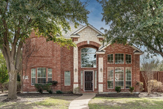 traditional home featuring stone siding, fence, and brick siding