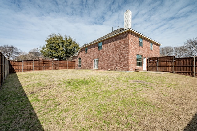 rear view of house featuring brick siding, a lawn, and a fenced backyard