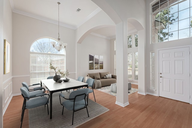 dining space with arched walkways, a towering ceiling, ornamental molding, an inviting chandelier, and light wood-style floors