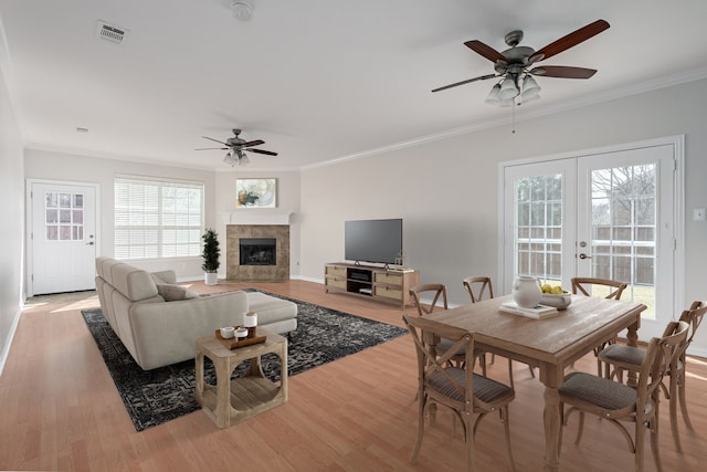 living area featuring french doors, crown molding, a tiled fireplace, a ceiling fan, and wood finished floors