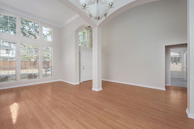 foyer entrance featuring light wood finished floors, baseboards, arched walkways, a towering ceiling, and a chandelier