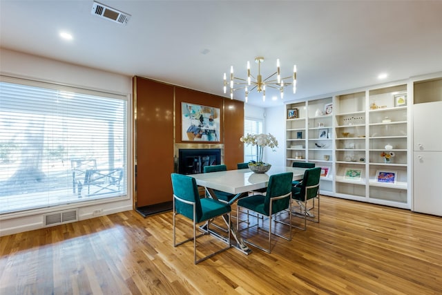 dining room featuring a glass covered fireplace, wood finished floors, visible vents, and a notable chandelier