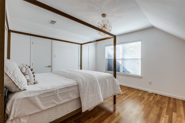 bedroom with a notable chandelier, visible vents, light wood-style flooring, vaulted ceiling, and baseboards