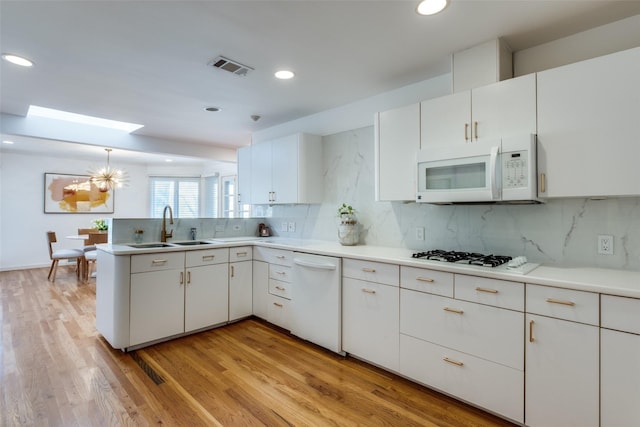 kitchen with white appliances, a skylight, visible vents, a peninsula, and a sink