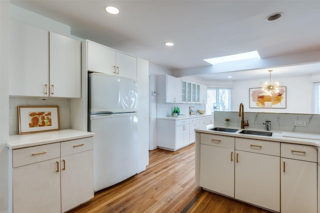 kitchen with a skylight, light wood-style flooring, freestanding refrigerator, white cabinetry, and a sink