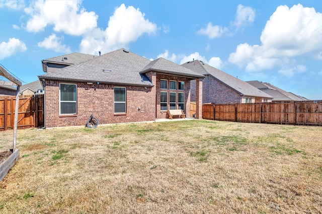 back of house featuring a yard, a fenced backyard, brick siding, and a shingled roof