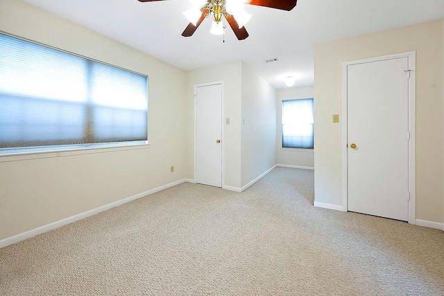 empty room with visible vents, baseboards, a ceiling fan, and light colored carpet